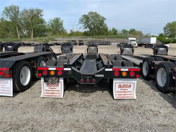 Lowboy trailer chassis and rear with multiple axles and signs in gravel lot.