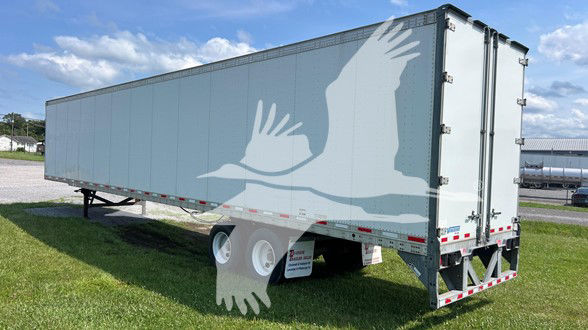 Trailer with side graphic of white birds in flight; long rectangular gray cargo trailer with dual rear doors and support legs