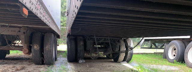 Trailer underside view showing axles and wheels of Vanguard VXP utility trailers, with dual rear axles and suspension components visible under the frame.