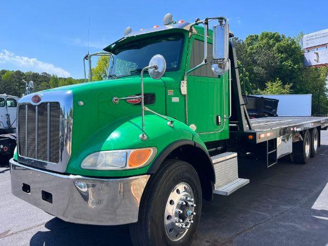 Green Peterbilt 348 rollback truck with chrome grille and flatbed, large side mirrors, and dual rear axles visible.