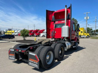 Volvo Daycab tractor rear and side showing chassis and wheels with red cab, 6x4 configuration, parking lot with other trucks in background.
