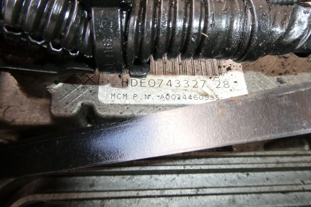 Label with serial number HDE0743327 28 and MCM P.N. A0024460935 surrounded by hoses and belt in an engine compartment.