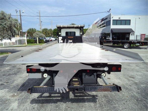 Flatbed tow truck with a lowered bed; rear view showing taillights, bumper, and ramps. I can see reflections and some labels on the equipment but no legible text clearly visible.