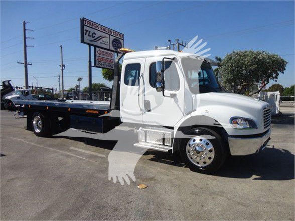 Flatbed tow truck side view showing cab and long flatbed, front grille, headlights, and chrome wheels.
