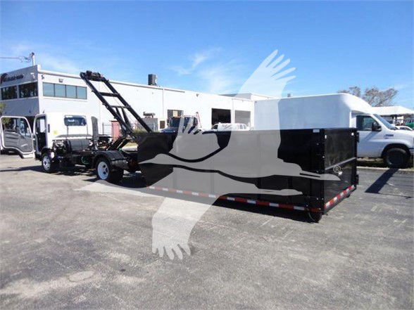 Isuzu NRR dump truck with large black and white trailer in a parking lot; image shows a car hauler or tow trailer attachment.