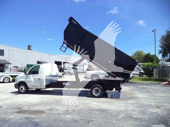 Ford E-450 dump truck with raised dump bed in a parking lot.