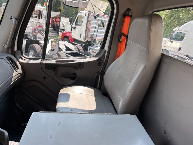 Cab interior of a 2015 Freightliner M2 chassis showing driver seat and passenger area, with a table/desk attached and orange seatbelt.