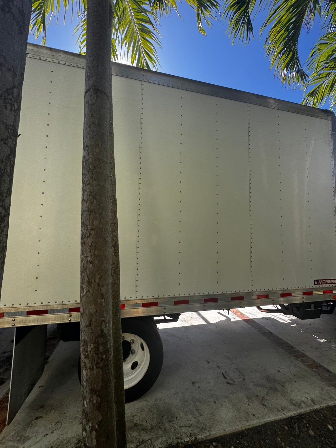 Box truck trailer with riveted side panels and Morgan brand sticker visible near rear bottom edge.