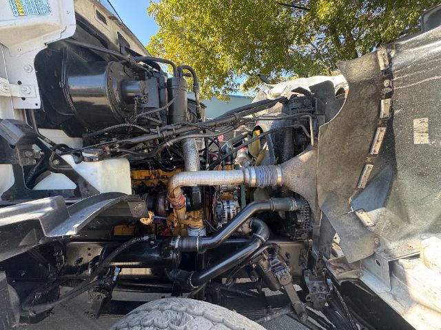 Vehicle engine bay of a 2006 Sterling L8500 vacuum truck showing visible hoses, metal piping, hydraulic lines, and engine components.