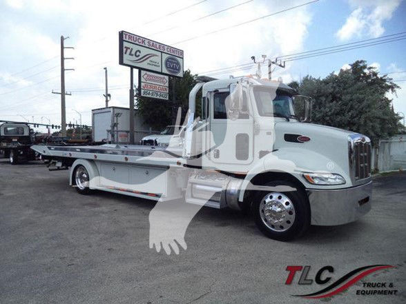 Tow truck with long wheelbase, Peterbilt logo on cab, TLC Truck & Equipment watermark, dealership sign in background, no visible vehicle text legible besides TLC logo.