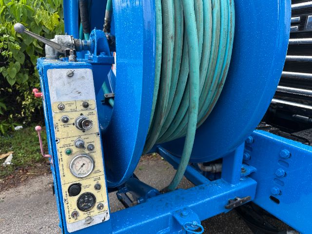 Blue industrial vacuum truck reel with hose and control panel showing gauge and switches.