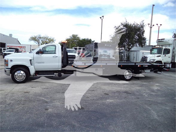2023 Chevrolet Silverado 6500HD tow truck chassis in a dealership lot showing front cab and extended flatbed with partial branding.