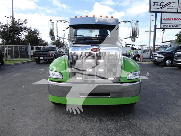 Front view of a green and silver Peterbilt 337 truck in a dealership lot, showing the chrome grille and emblem, large side mirrors, and headlights.