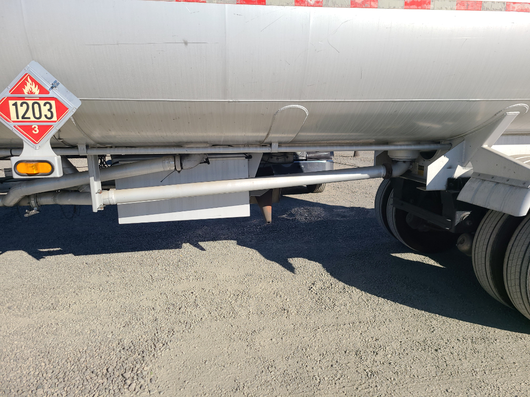 Beall semi trailer side view showing hazardous materials placard 1203 and undercarriage with suspension and wheels.