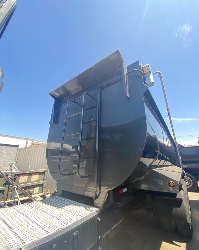 Peterbilt 365 dump truck with raised dump bed and rear ladder, visible wheel and metal ramp.