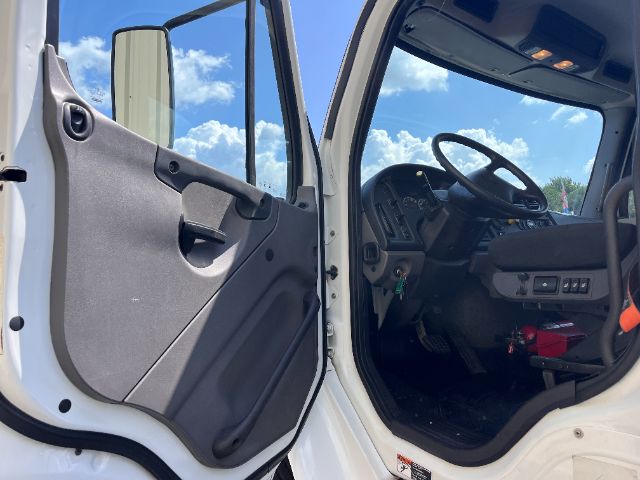 Cab interior of a Freightliner M2 truck showing the driver's door open, steering wheel, dashboard controls, and entry area.