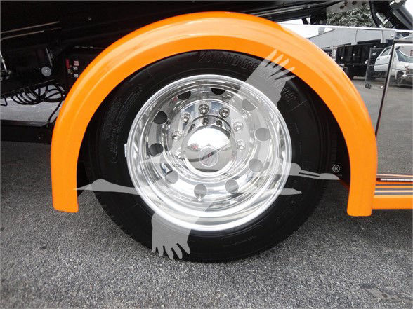 Wheel well of a 2022 Peterbilt 337 with bright orange fender and polished chrome wheel; tire brand and wheel details partially visible.