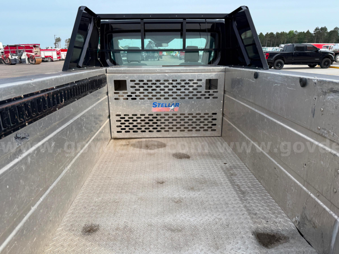 Truck bed of a 2016 Ford Transit Stellar service utility with perforated metal bulkhead and logo; metal diamond plate floor with dirt marks; rear cab view.