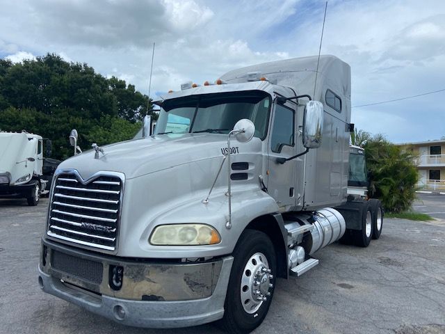 Truck cab in silver with sleeper, front grille, large mirrors, and dual rear axles. shows Mack CXU613 style conventional sleeper semi-truck.