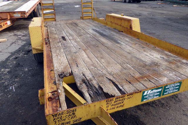 Cam Warrior trailer deck showing wooden planks and yellow steel frame with warning labels and stickers along edge.