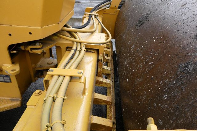 Bomag BW212D-2 compacting drum and hydraulic hoses on the right side of the machine with yellow body and large steel wheel in contact.