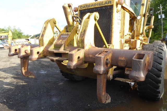 Front view of a Caterpillar 16G motor grader with a three-point hitch and hooks, showing yellow paint and rust on implement pins.