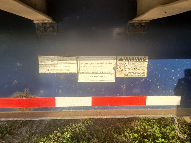 Trailer undercarriage with warning labels and decals on blue frame; red/white reflective strip at bottom; three rectangular labels in the center.