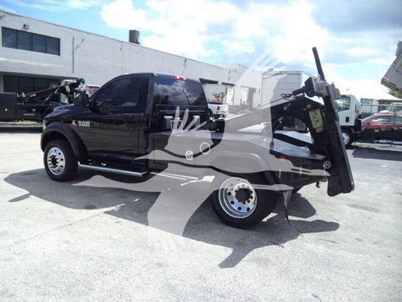 Ram 4500 tow truck with hydraulic tilt bed in black, rear view showing wheel and hydraulic mechanism.
