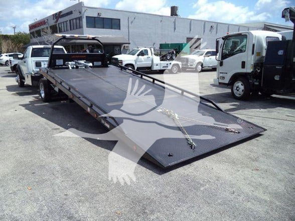 Ram 5500 tow truck flatbed with steel ramp, front winch, and surrounding lot of trucks.