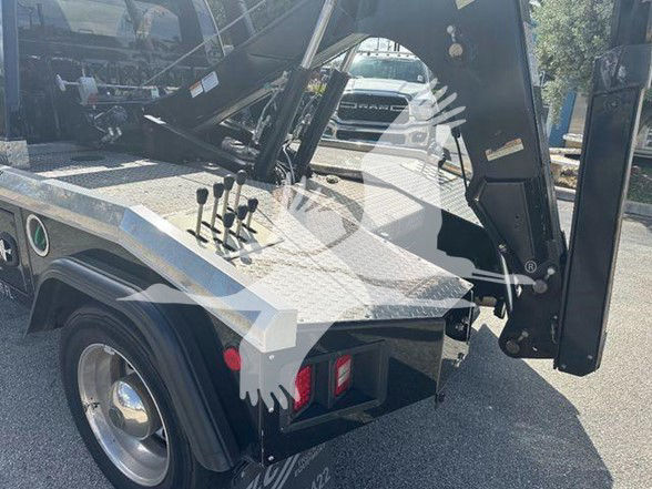 Tow truck rear section showing hydraulic controls and flatbed platform with lettering and a red tail light.