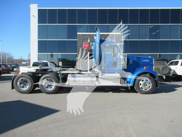 Kenworth W900L conventional daycab truck side view showing chrome fuel tanks and blue cab with dual rear axles.