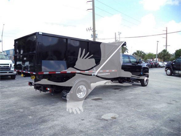 Truck with a large black dump bed or trailer attached to a cab, viewed from rear-left side in a parking lot.