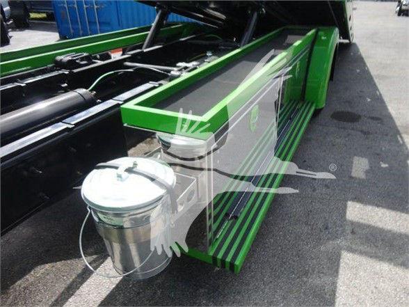 Green International MV truck bed with fuel tank and storage step; visible components include a polished metallic cylindrical fuel/air tank mounted under a green side step, hydraulic lines, and a black chassis frame.