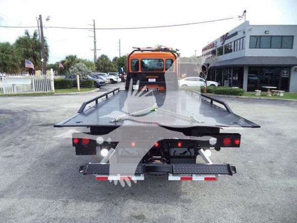 Tow truck flatbed rear view with orange cab, loading ramps, and platform ready for vehicle haul.