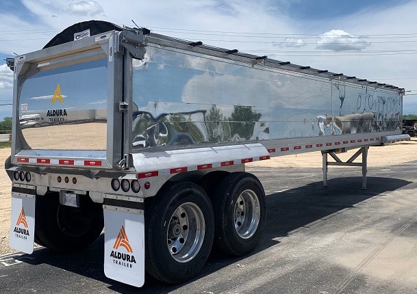 Side view of a 2025 aluminum end dump trailer with dual axles, polished reflective sides, and Aldura Trailer branding.