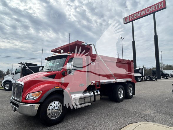 Kenworth T480 dump truck in red with a dumping bed, parked on pavement near a Kenworth dealership sign.