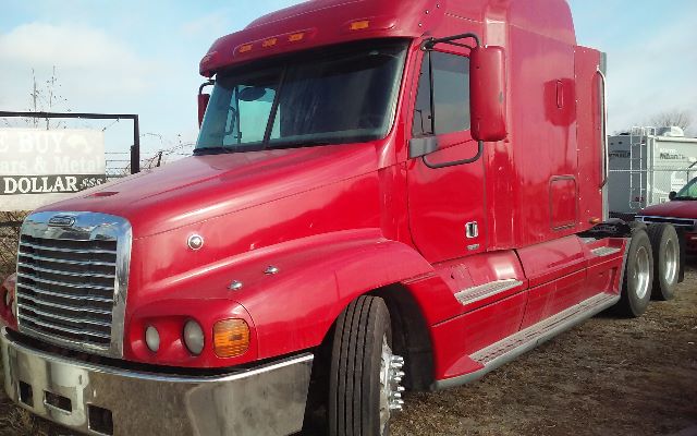 Red Freightliner conventional sleeper tractor showing front grille and side steps, with dual rear wheels and large cab.