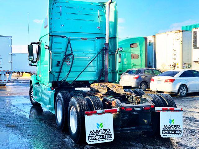 Truck tractor rear/side view showing fifth wheel, dual rear axles, and green exterior with white rear mudflaps displaying Macro Truck Sales contact.