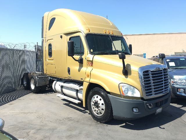 Truck cab of a 2010 Freightliner Cascadia 125 with beige/gold color, front grille, two fuel tanks, and a chassis behind the cab. Visible text: none obvious on the vehicle itself.