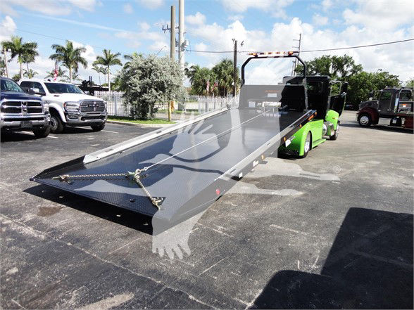 Tow truck flatbed chrome steel truck bed with hydraulic tilt on a green tow tractor and Palms in background.