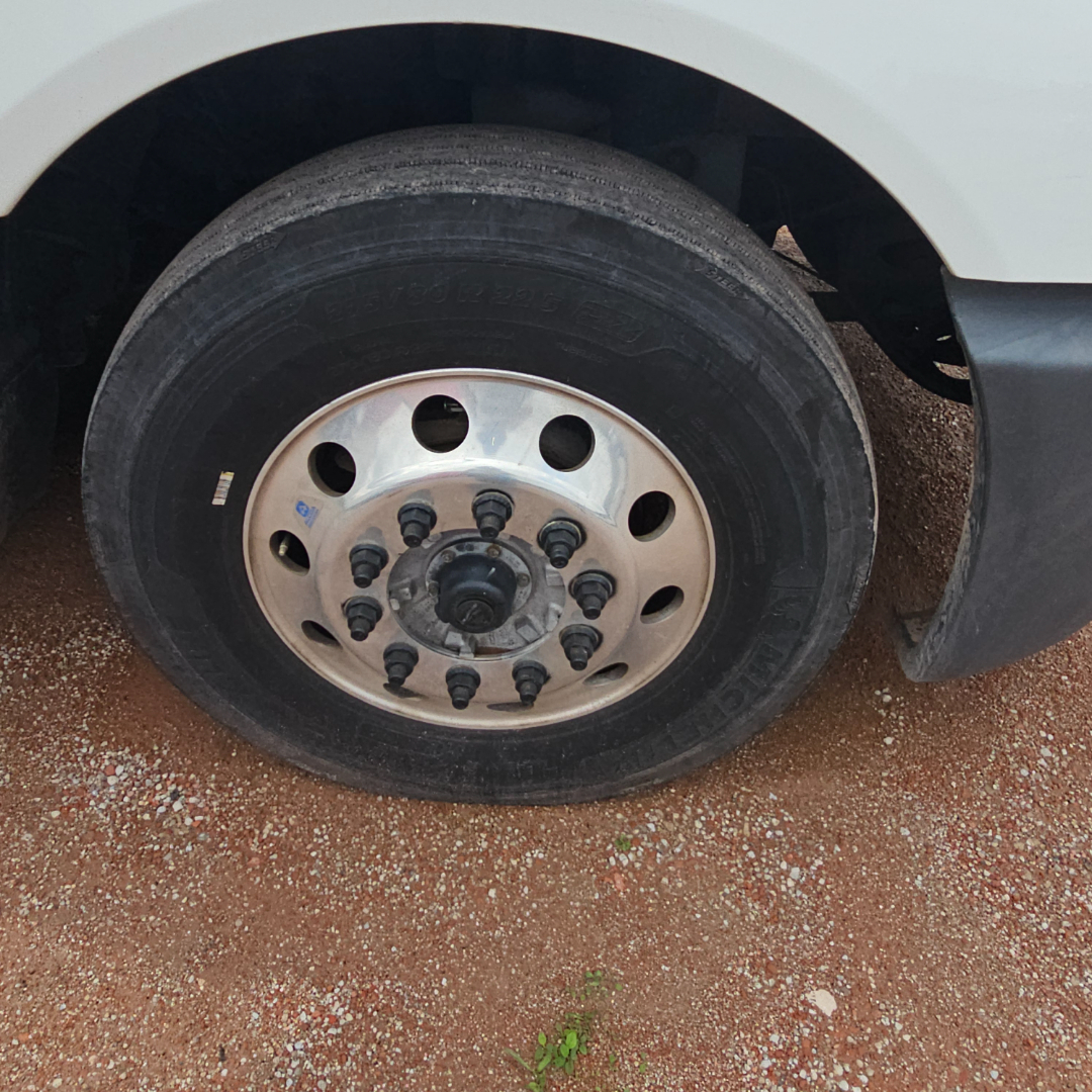 Truck wheel with polished steel rim and black lug nuts on a tire, showing hub area and wheel well.