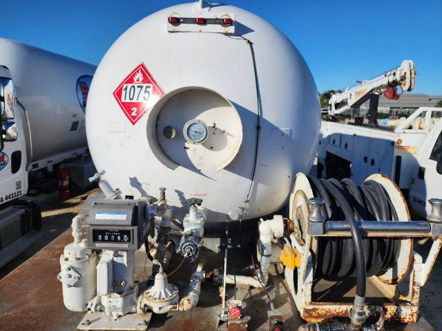 Truck equipment showing a white cylindrical tank with hazard label 1075-2, hoses, reels, and control panel mounted on a frame.