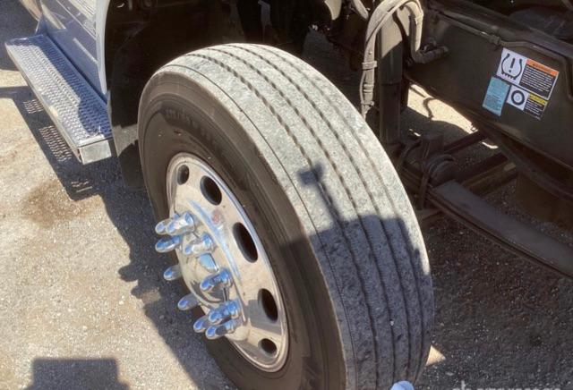 Truck front wheel and steering area showing dual rear axles and wheel with multiple lug nuts; metallic hub with circular holes.