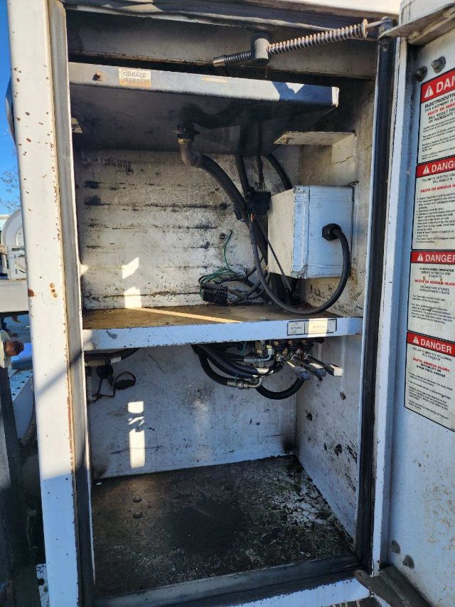 Ford F550 truck aerial lift compartment showing control box, hydraulic hoses, and wiring harness inside a metal storage bay.