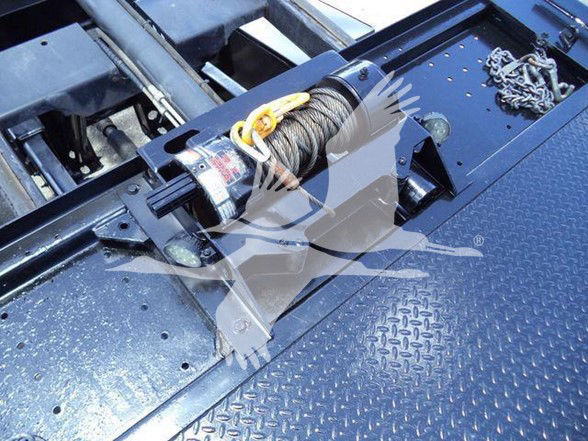 Tow truck winch assembly on diamond plate deck with hook and cable reel visible.
