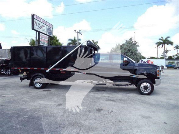 2023 International CV refuse truck with dump bed, black cab, and white lettering. Visible signage in background includes TLC and FedEx logos. Side of truck shows dump bed and hydraulic mechanism.