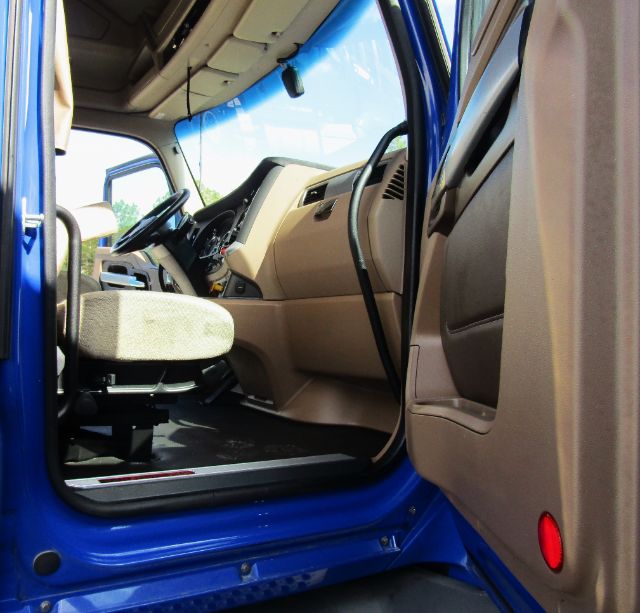 Internal view of a blue 2020 Kenworth T680 cab showing beige dashboard, steering wheel, and driver's seat from the door opening.