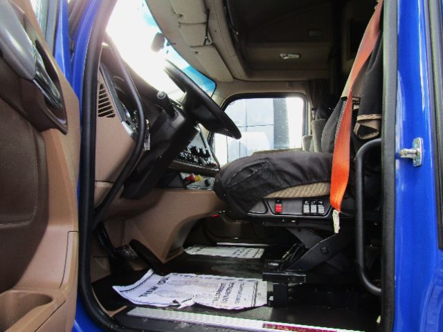 Cab and dashboard area of a 2020 Kenworth T680 inside cabin view showing driver seat with orange seat belt and steering wheel.