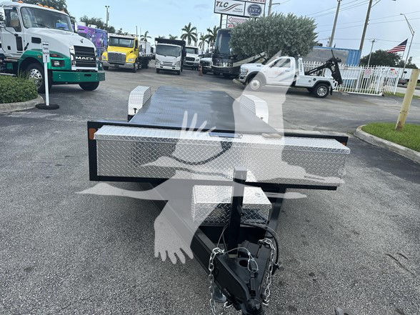 Flatbed trailer with a diamond plate toolbox/front tongue area; hitch and safety chains visible; background shows dealership lot with trucks. Text on image not clearly legible.