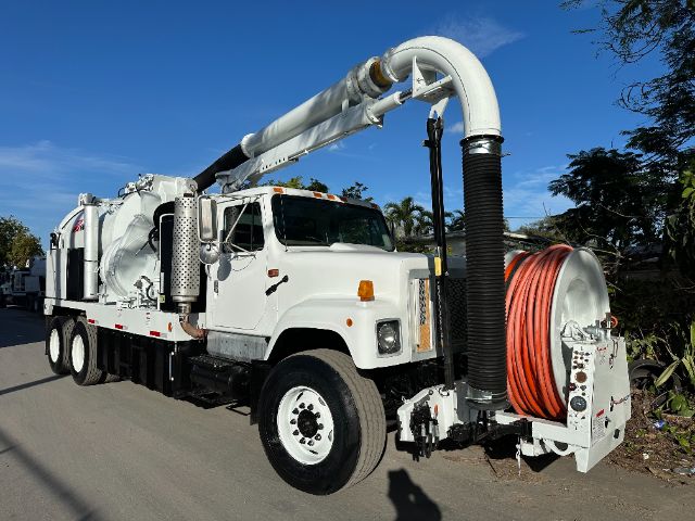 International vacuum truck with large white cab and orange hose reel, equipped with a long gray vacuum boom and black intake hose.